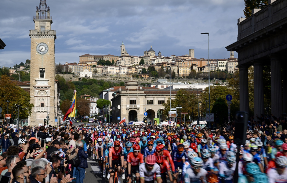 Maratona de ciclismo em Torino, com centenas de ciclistas participando na cidade histórica, cercada por edifícios antigos e com uma praça emblemática ao fundo.