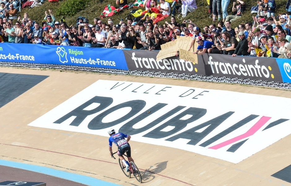 Ciclismo na Velódromo Ville de Roubaix, na França, durante a famosa corrida de ciclismo Paris-Roubaix, com público assistindo do alto das arquibancadas.