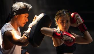 Mulher treinando boxe com personal trainer na academia, usando luvas de boxe vermelhas e treinando socos precisos.