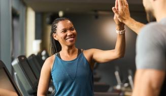 Mulher sorridente em treino na academia dando high five para seu treinador, demonstrando motivação e bem-estar na prática de exercícios físicos.