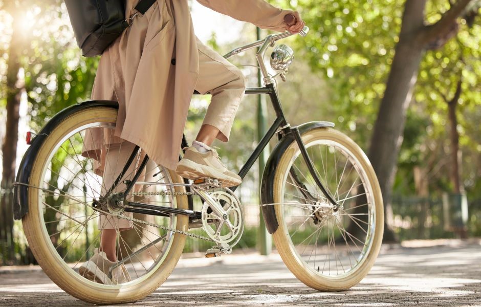 Pessoa pedalando uma bicicleta preta com rodas bege em um parque com árvores e luz natural, desfrutando de um passeio ao ar livre.
