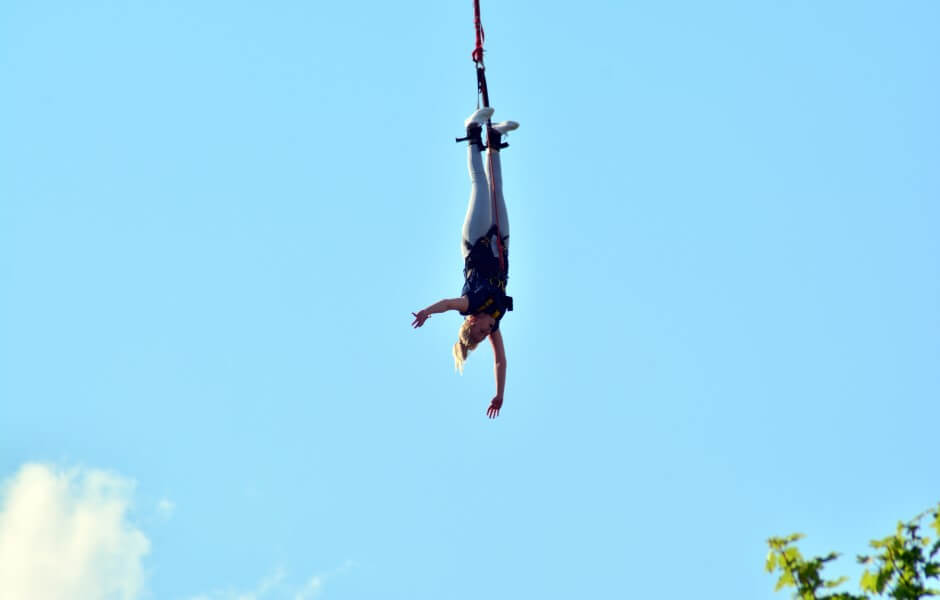 Imagem de uma praticante de bungee jump, pendurada de cabeça para baixo por uma corda presa aos seus pés.