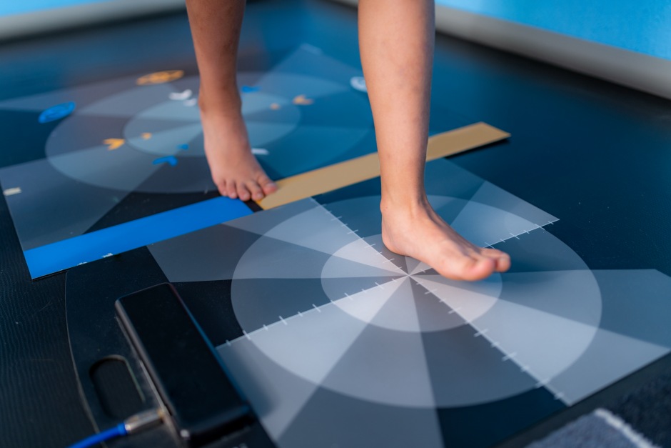 Pessoa testando um dispositivo de equilíbrio com os pés, destacando o uso de tecnologia de medição de movimento e equilíbrio.