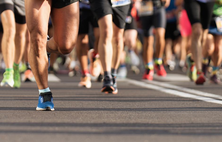 Imagem de corredores em uma maratona, destacando as pernas enquanto eles aceleram na pista. A energia e a determinação dos participantes são visíveis.