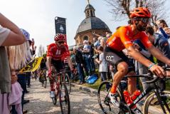 Atletas profissionais de ciclismo competindo em uma corrida oficial com uma multidão de espectadores apoiando ao lado de uma igreja histórica ao ar livre.