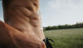 Imagem de um homem em forma exibindo seu abdômen definido em um ambiente externo.