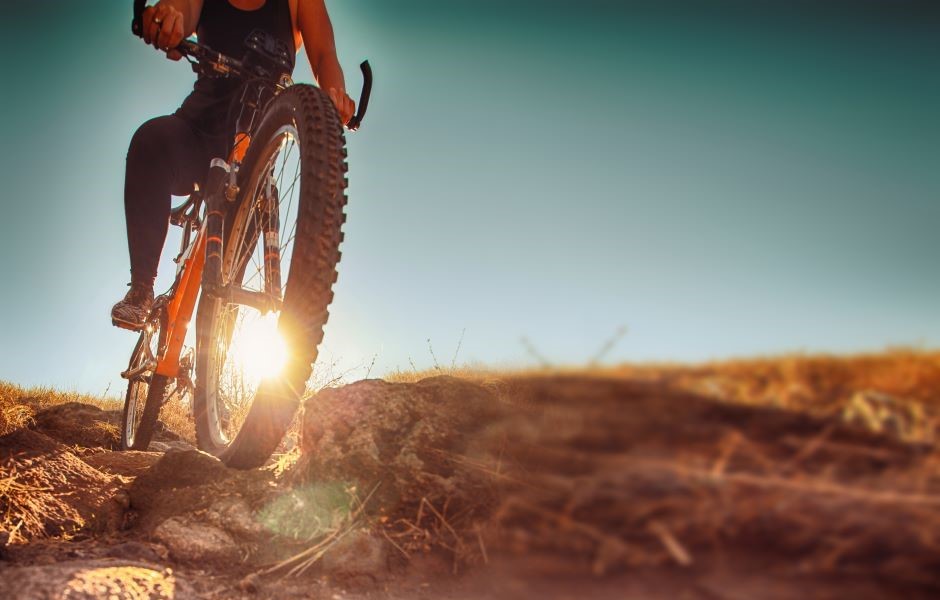 Pessoa pedalando uma mountain bike em trilha de terra ao pôr do sol, explorando trilhas off-road de forma aventureira e emocionante.