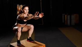 Mulher realizando agachamento em uma caixa, com foco na postura e técnica de treino em ambiente de academia.