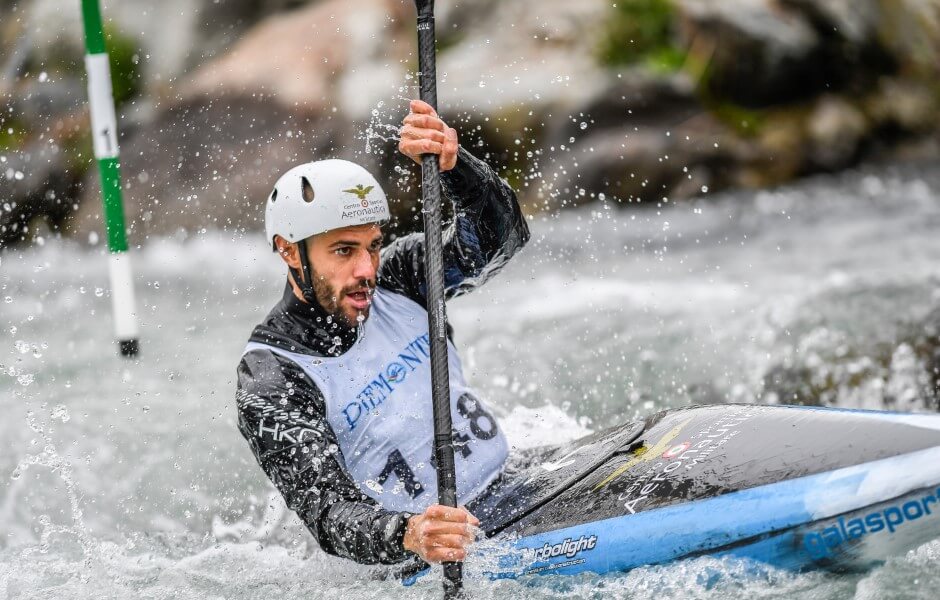 Imagem de um atleta de canoagem, ele segura um remo com as duas mãos e olha determinado para frente.