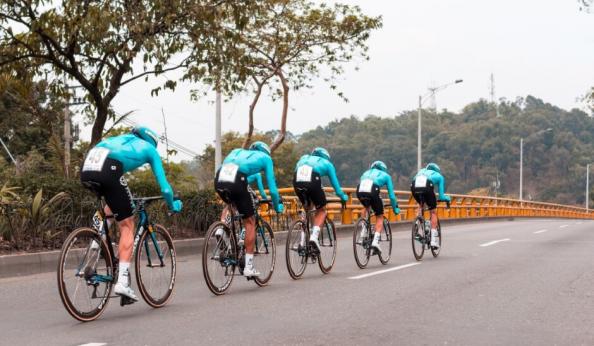 Ciclistas em ação em uma estrada, todos vestidos com camisetas azuis. A imagem captura um momento dinâmico da prática de ciclismo em equipe.