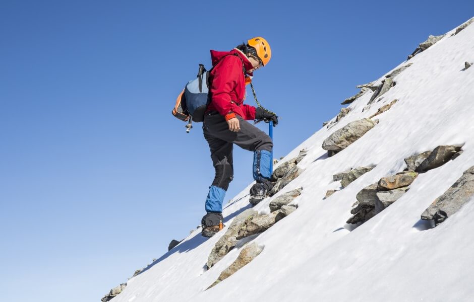 Imagem de uma mulher escalando uma montanha coberta de gelo, utilizando equipamentos de segurança adequados para a atividade.