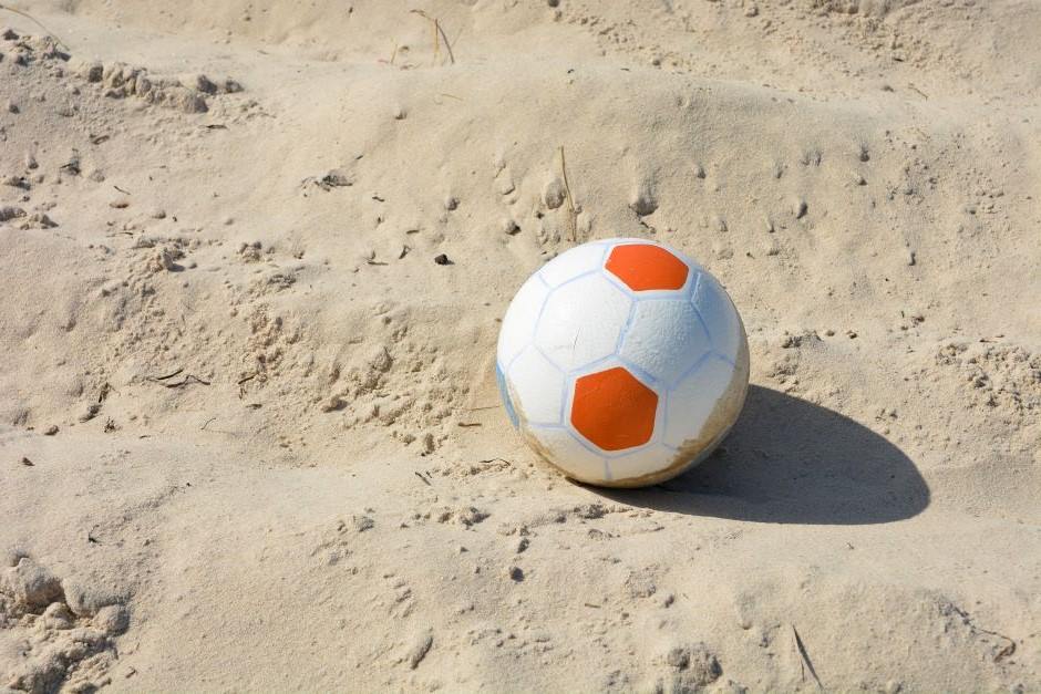 Bola de futebol de areia, nas cores branca e laranja, sobre a areia