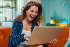 Mulher sorridente usando um laptop em casa, com expressão de felicidade, representando sucesso, inovação, tecnologia e rotina diária em ambiente moderno.