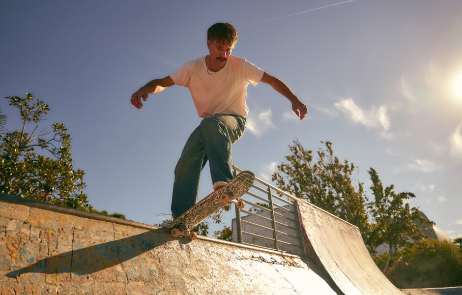 Imagem de um skatista realizando uma manobra em uma pista de skate, em um dia ensolarado.