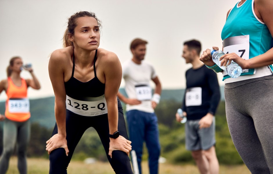 Imagem de um grupo de pessoas ao ar livre em uma área gramada, todos vestidos com roupas esportivas e usando números. Eles participam de um evento de corrida.