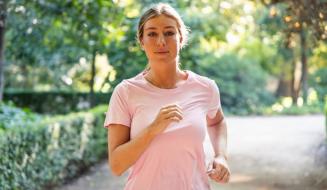 Mulher correndo ao ar livre em parque com árvores verdes na primavera, usando camiseta rosa, demonstrando saúde e bem-estar.