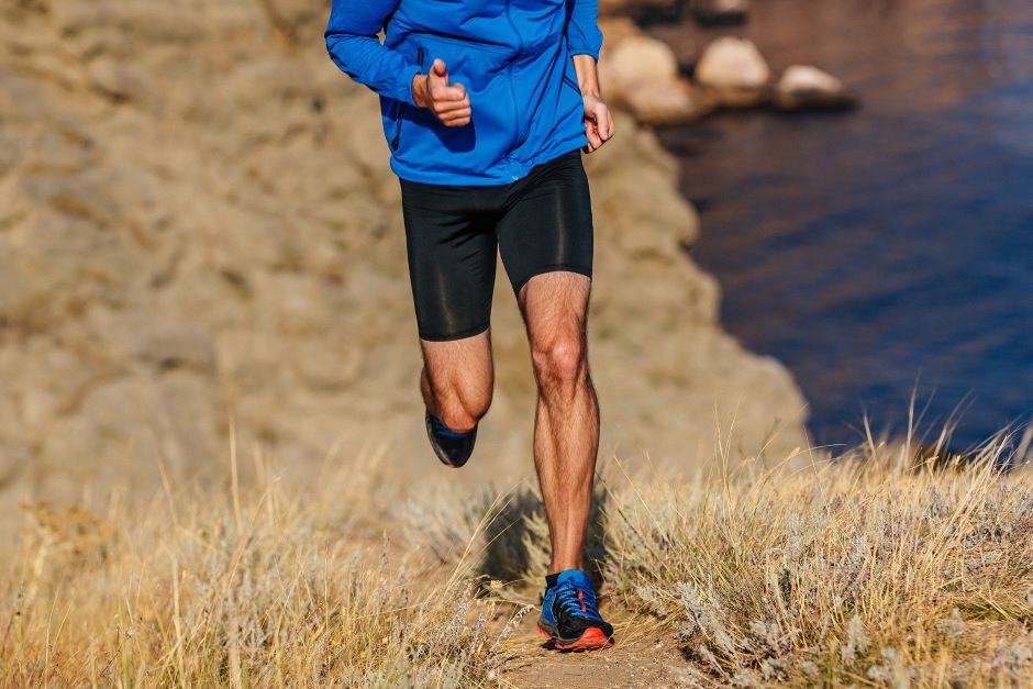 Tronco e pernas de um atleta correndo a beira de um lago