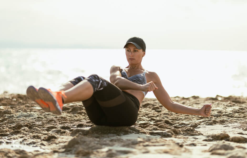 Foto de uma mulher na praia realizando um exercício para fortalecer o core.