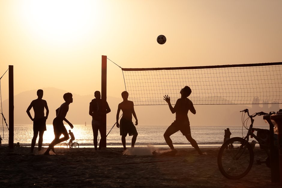 Grupo de pessoas jogando futevôlei na praia, mar e sol ao fundo