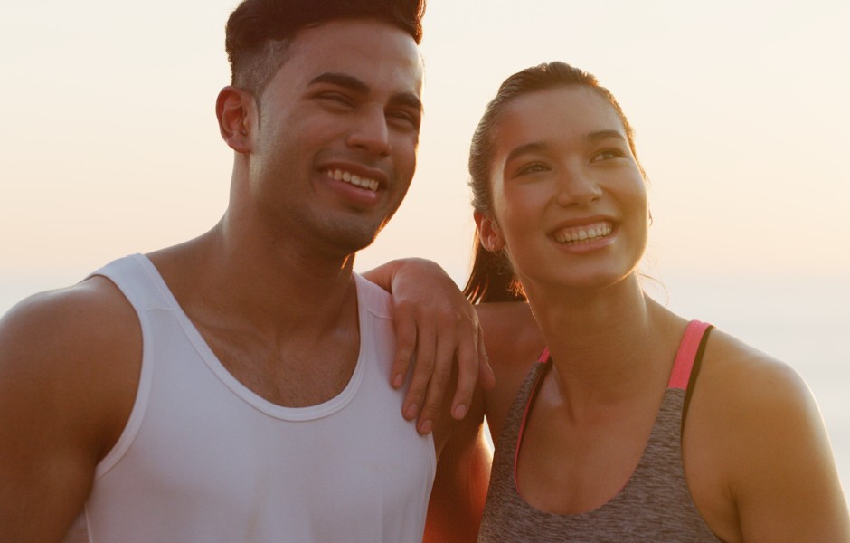 Casal sorridente ao ar livre, aproveitando um momento juntos em um cenário ensolarado, refletindo felicidade e companheirismo.