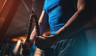 Homem com camiseta azul treinando força com corda de resistência na academia, focado e determinado na atividade de exercícios físicos para hipertrofia muscular.