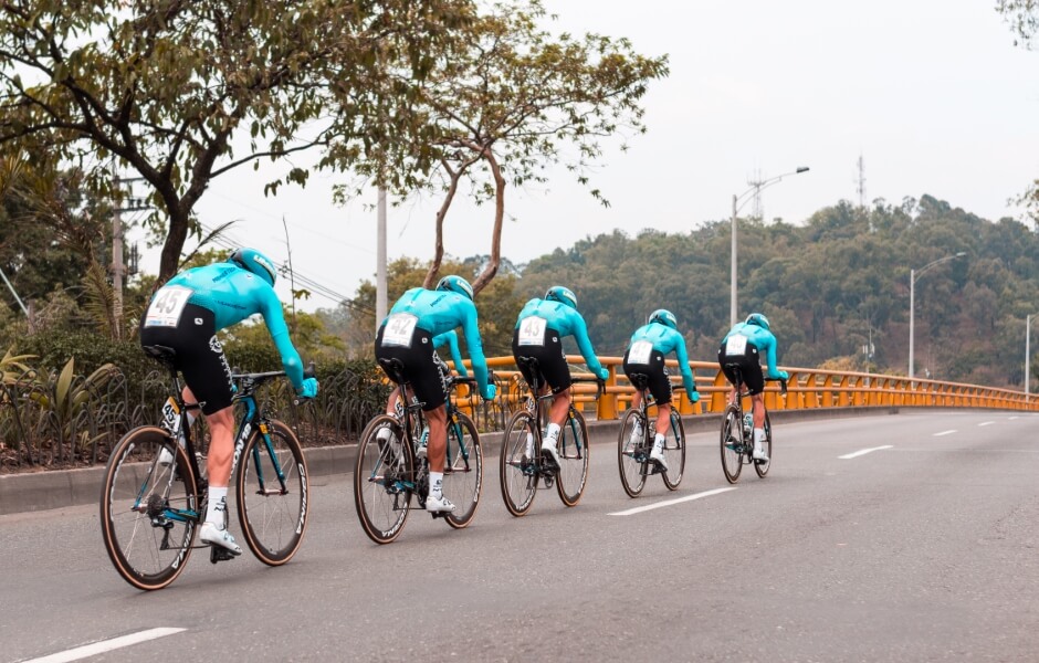 Ciclistas em ação em uma estrada, todos vestidos com camisetas azuis. A imagem captura um momento dinâmico da prática de ciclismo em equipe.