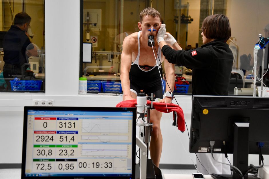 Atleta realizando teste de resistência em laboratório de performance física, monitorado por especialista durante avaliação esportiva.