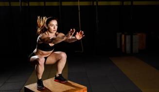 Mulher realizando agachamento em uma caixa, com foco na postura e técnica de treino em ambiente de academia.