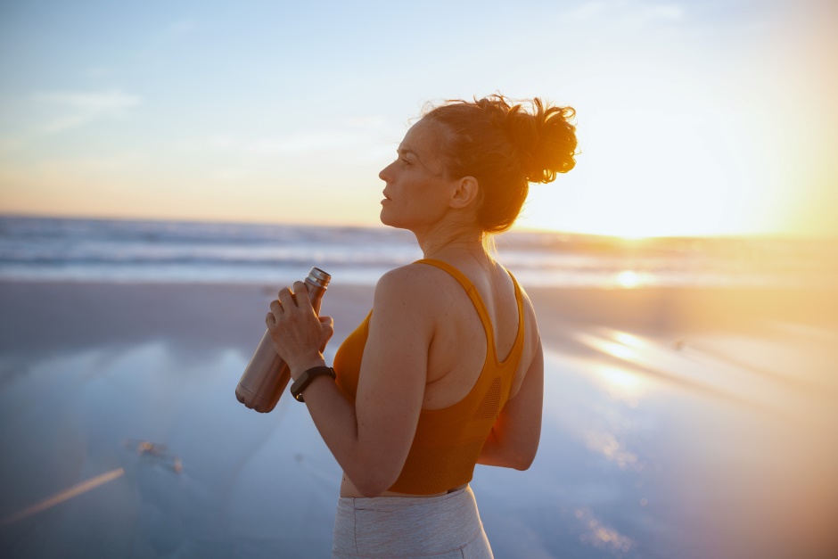 Uma mulher na beira da praia com uma garrafa de água na mão