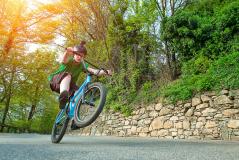 Criança praticando manobras em uma bicicleta em um caminho rodeado pela natureza durante um dia ensolarado