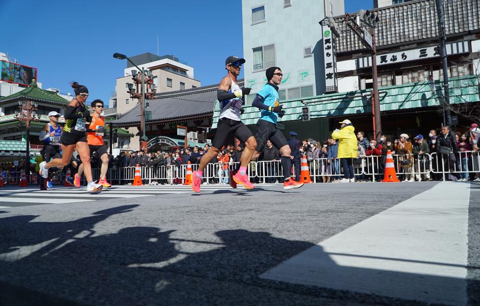 Corredores participam de uma emocionante maratona em dia ensolarado, com multidão vibrante ao fundo, mostrando energia e determinação na corrida.