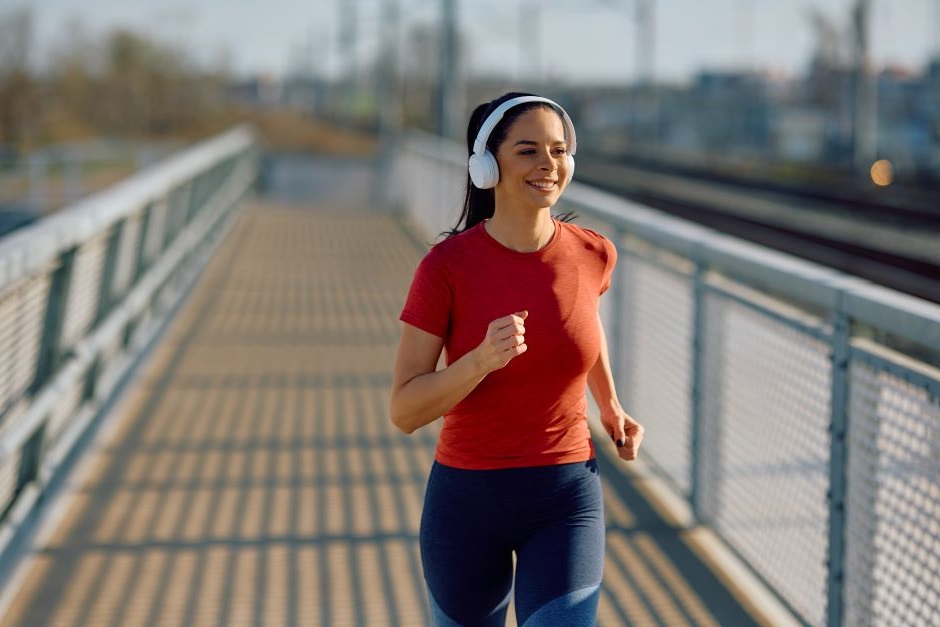 Mulher correndo com roupas de ginástica e fones de ouvido. A mulher corre em uma ponte.