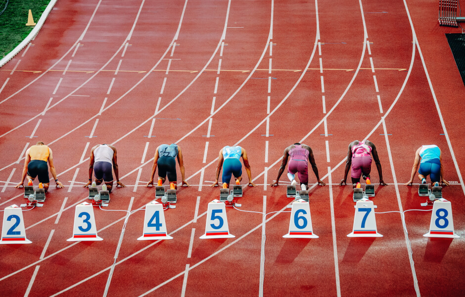 Imagem de uma pista de atletismo com vários atletas em posição, aguardando a largada.