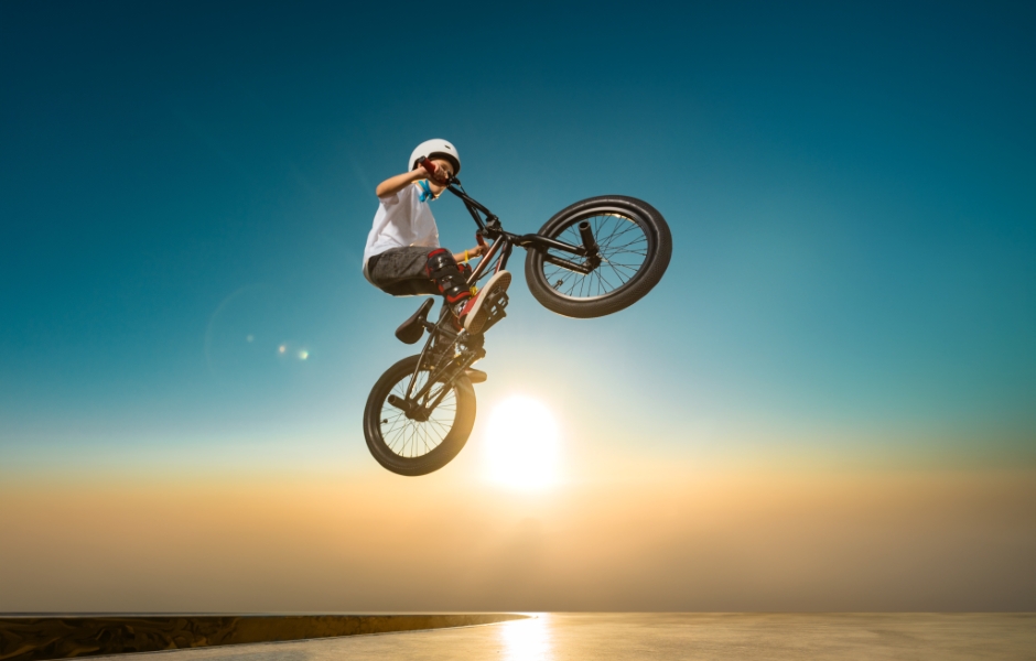 Um jovem fazendo acrobacias com sua bicicleta BMX durante o pôr do sol, destacando a adrenalina e a habilidade do ciclismo em BMX