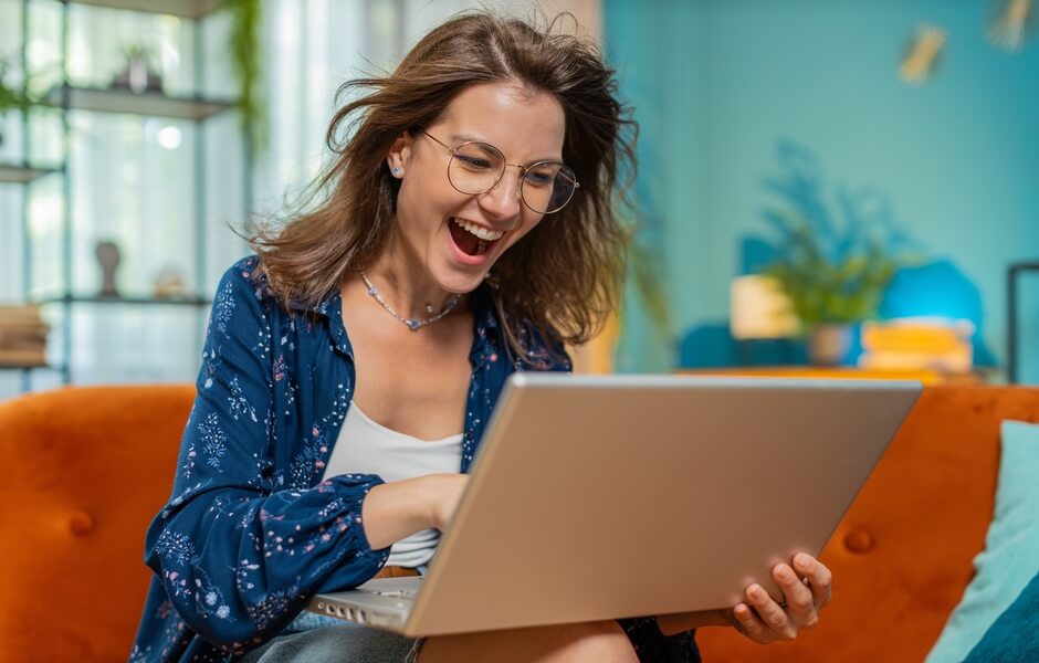 Mulher sorridente usando um laptop em casa, com expressão de felicidade, representando sucesso, inovação, tecnologia e rotina diária em ambiente moderno.