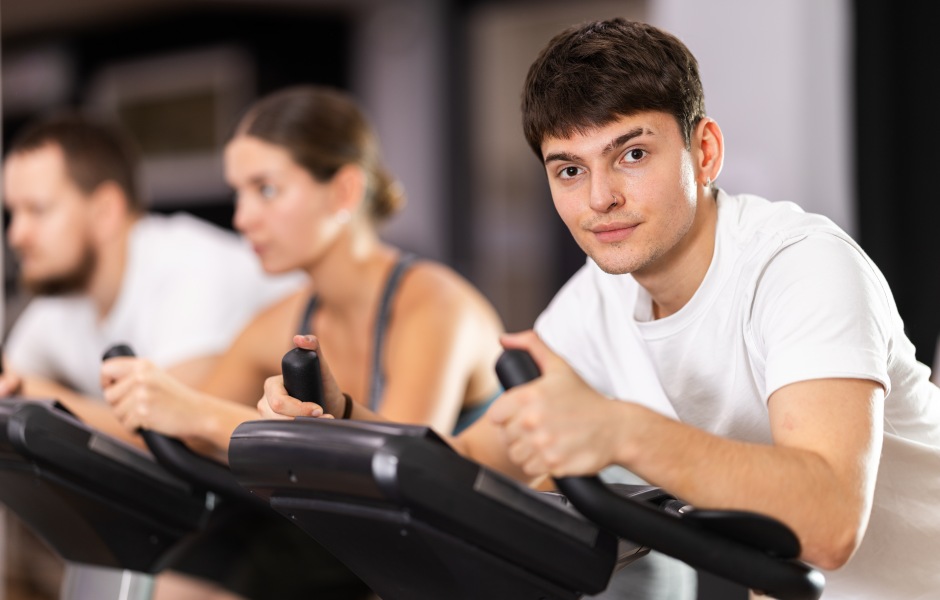 Três jovens fazendo exercício em bicicletas ergométricas em uma academia.