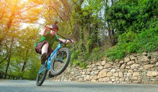 Criança praticando manobras em uma bicicleta em um caminho rodeado pela natureza durante um dia ensolarado