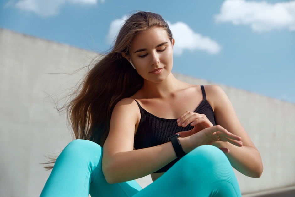Jovem mulher ao ar livre com roupas de fazer exercícios físicos olhando para seu relógio.