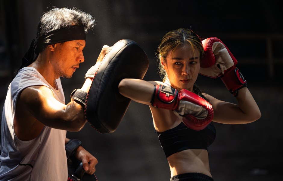 Mulher treinando boxe com personal trainer na academia, usando luvas de boxe vermelhas e treinando socos precisos.