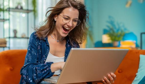 Mulher sorridente usando um laptop em casa, com expressão de felicidade, representando sucesso, inovação, tecnologia e rotina diária em ambiente moderno.