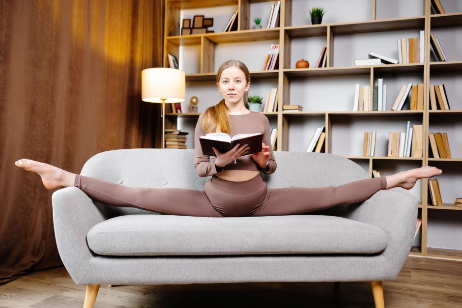 Imagem de uma mulher fazendo um split em cima de uma poltrona enquanto lê um livro