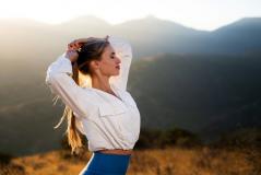 Mulher jovem praticando yoga ao ar livre ao entardecer, com montanhas ao fundo e iluminação natural suave, promovendo bem-estar e conexão com a natureza.