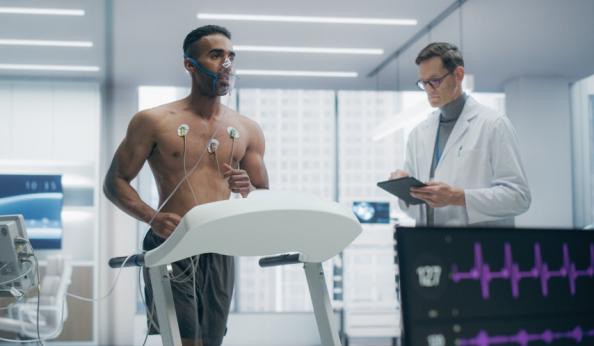 Paciente masculino realizando testes cardíacos com eletrodos no peito sob supervisão de um médico em laboratório de medicina esportiva.