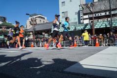 Corredores participam de uma emocionante maratona em dia ensolarado, com multidão vibrante ao fundo, mostrando energia e determinação na corrida.