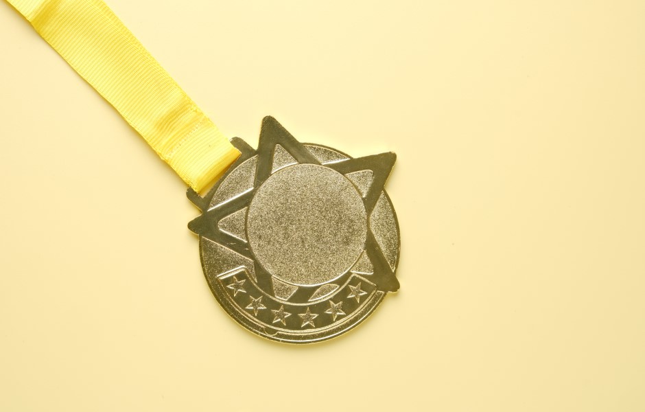 Imagem de uma medalha dourada em formato de estrela, com uma fita amarela.