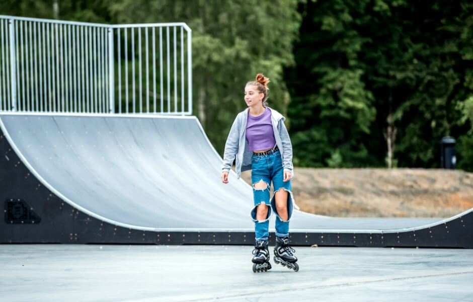 Imagem de uma jovem andando de roller em um ambiente externo, com uma pista de skate ao fundo.