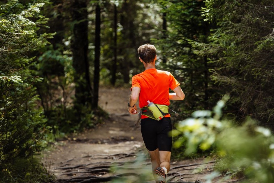 Imagem de um homem correndo em uma floresta com um cinto específico para corrida que suporta sua garrafa d'água.