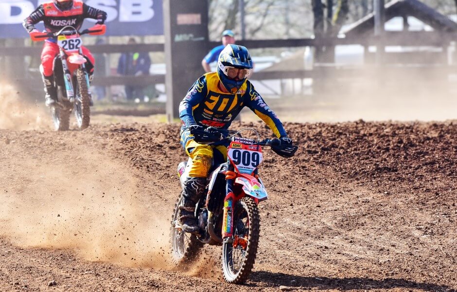 Imagem de um motoqueiro participando de uma corrida de motocross em uma pista de terra, usando capacete e roupas de segurança.