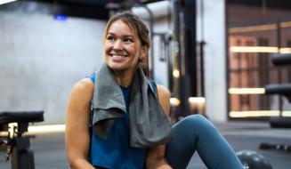 Mulher sorridente no supermercado com roupas esportivas, segurando um celular, após treino ou atividade física, ambiente moderno e bem iluminado.