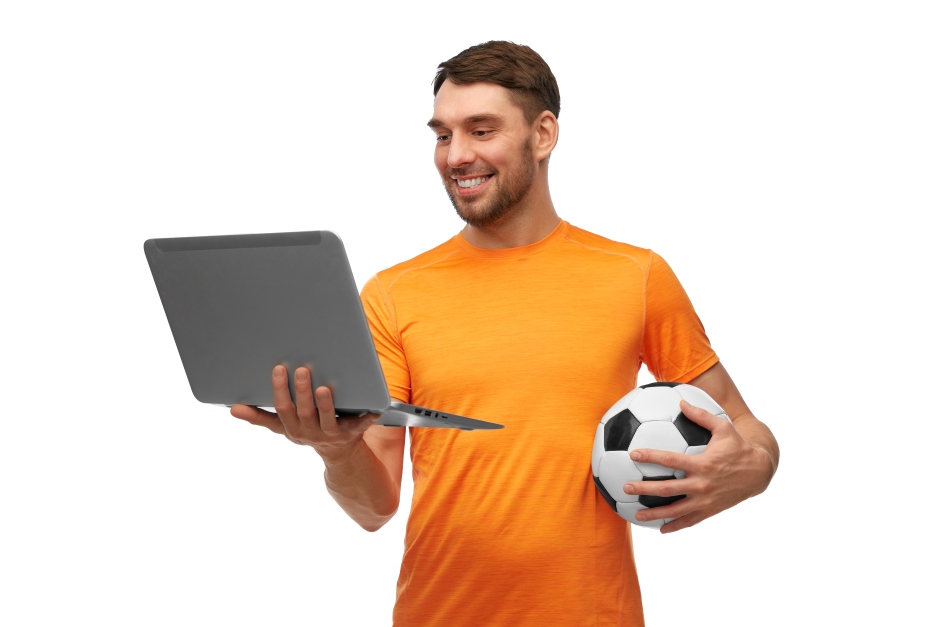 Um homem sorrindo enquanto segura uma bola de futebol e um laptop